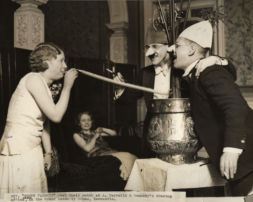 Two men in false noses and cigarette holders laugh at a woman blowing a party streamer: credit Newcastle Libraries Public domain
